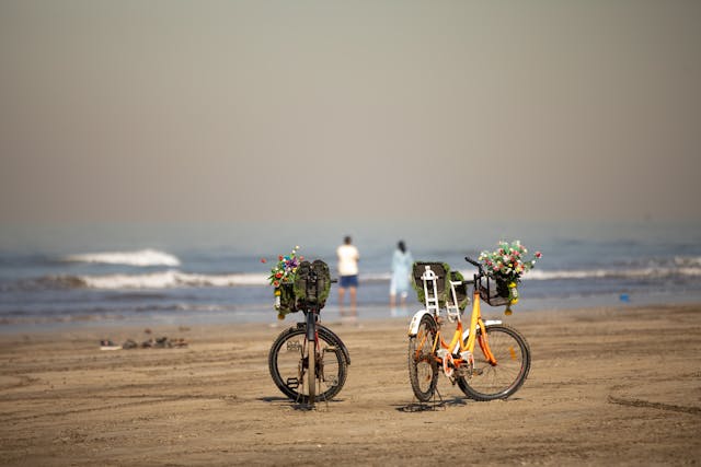 Two bikes parked on a sandy beach, with the ocean waves in the background. Ideal for exploring the best bike routes in San Francisco.