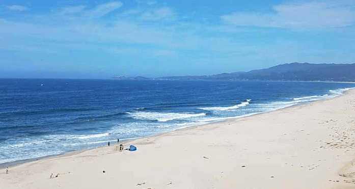 A sunny beach in Northern California with people enjoying the sand and a majestic mountain in the backdrop.